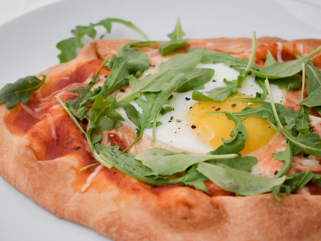 Breakfast pizza on naan with an egg and arugula