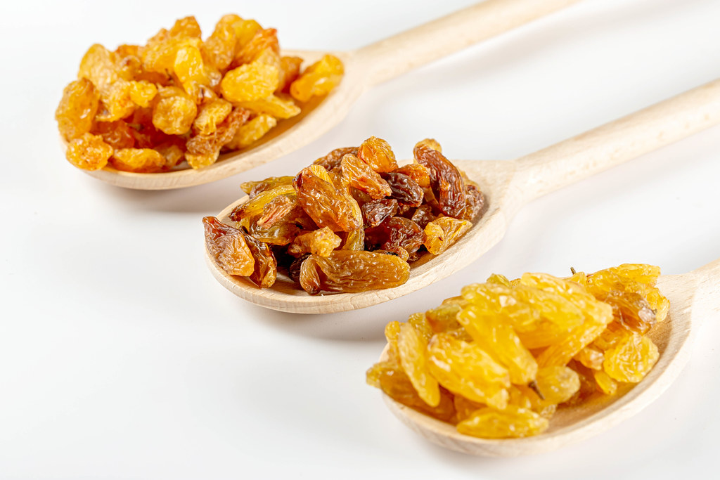 close up of three kinds of raisins on spoons