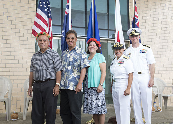 Micronesians standing with U.S. armed forces members in front of several flags