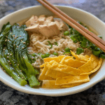 bowl of ramen with eggs, bok choy, and chicken with chopsticks