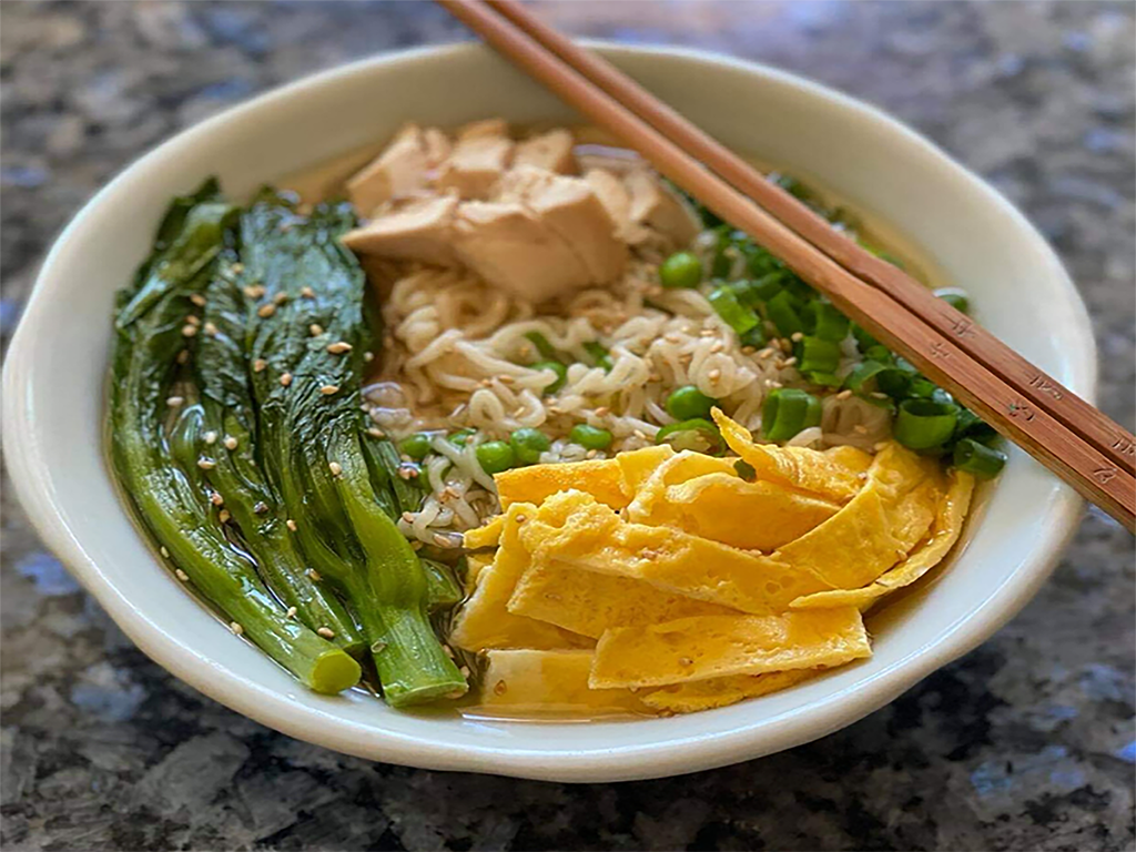 bowl of ramen with eggs, bok choy, and chicken with chopsticks