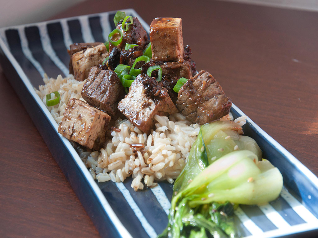rectangular plate with beef and tofu over brown rice with bokchoy and green onion garnish