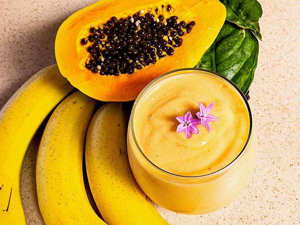 smoothie garnished with purple flowers and bananas, cut papaya, and leaves as accent