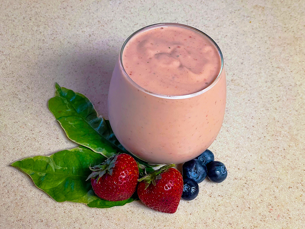 Poi fruit smoothie in clear glass with leaves, strawberries, and blueberries as an accent