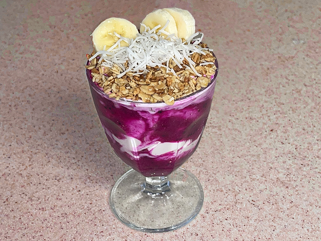 Dragon fruit and yogurt bowl in glass cup with granola and toasted coconut flakes on top with banana slices
