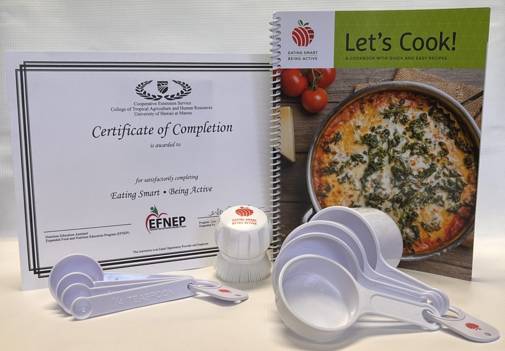 Certificate of Completion, ESBA cookbook, measuring cups and spoons, and a produce scrub brush on a table.