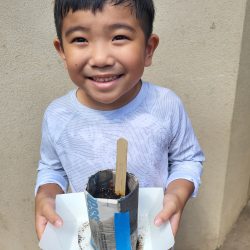 Child posing with newspaper pot with bok choy seeds planted