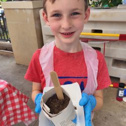 Child posing with newspaper pot with bok choy seeds planted