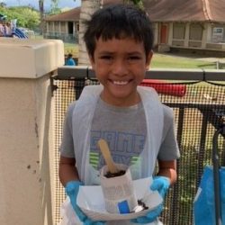 Child posing with newspaper pot with bok choy seeds planted