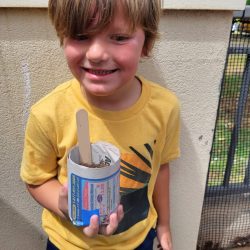 Child posing with newspaper pot with bok choy seeds planted