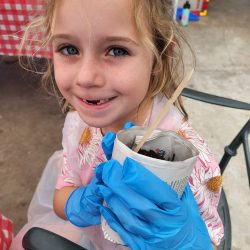 Child posing with newspaper pot with bok choy seeds planted