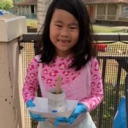 Child posing with newspaper pot with bok choy seeds planted