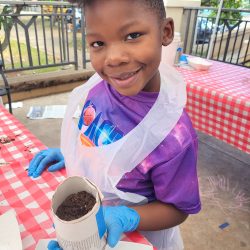 Child posing with newspaper pot with bok choy seeds planted