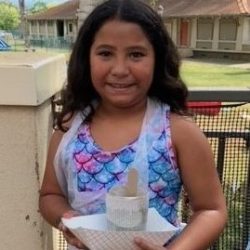 Child posing with newspaper pot with bok choy seeds planted