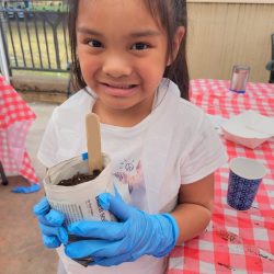 Child posing with newspaper pot with bok choy seeds planted