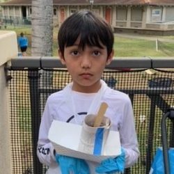 Child posing with newspaper pot with bok choy seeds planted