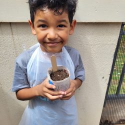 Child posing with newspaper pot with bok choy seeds planted