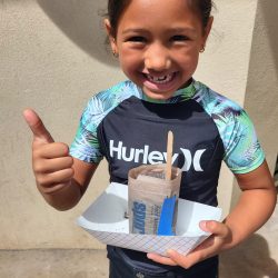 Child posing with newspaper pot with bok choy seeds planted