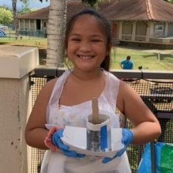 Child posing with newspaper pot with bok choy seeds planted