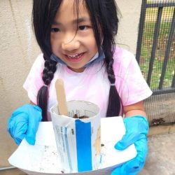 Child posing with newspaper pot with bok choy seeds planted