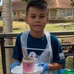 Child posing with newspaper pot with bok choy seeds planted