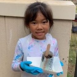 Child posing with newspaper pot with bok choy seeds planted