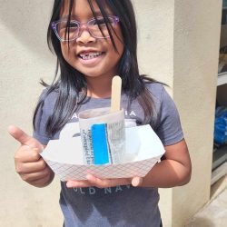 Child posing with newspaper pot with bok choy seeds planted