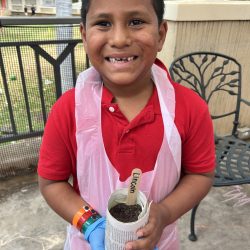 Child posing with newspaper pot with bok choy seeds planted