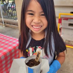 Child posing with newspaper pot with bok choy seeds planted