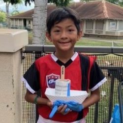 Child posing with newspaper pot with bok choy seeds planted