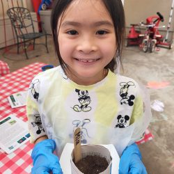 Child posing with newspaper pot with bok choy seeds planted