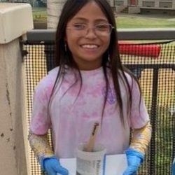 Child posing with newspaper pot with bok choy seeds planted