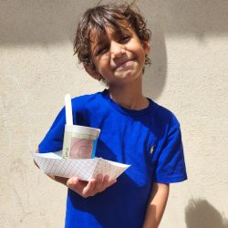 Child posing with newspaper pot with bok choy seeds planted