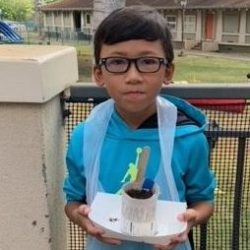 Child posing with newspaper pot with bok choy seeds planted