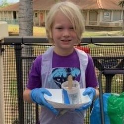 Child posing with newspaper pot with bok choy seeds planted