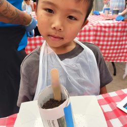 Child posing with newspaper pot with bok choy seeds planted