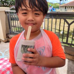 Child posing with newspaper pot with bok choy seeds planted