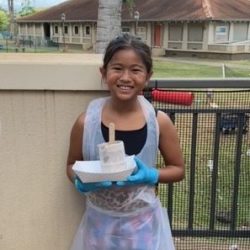 Child posing with newspaper pot with bok choy seeds planted