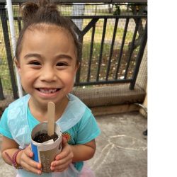 Child posing with newspaper pot with bok choy seeds planted