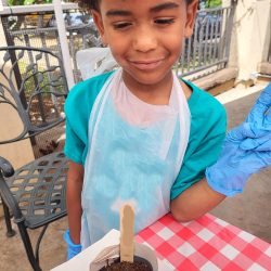 Child posing with newspaper pot with bok choy seeds planted