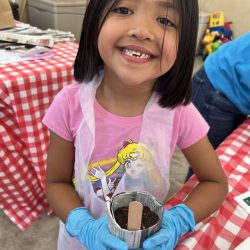 Child posing with newspaper pot with bok choy seeds planted