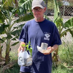 Participant posing with newspaper pot with seeds planted inside and transplanted green bean seedling