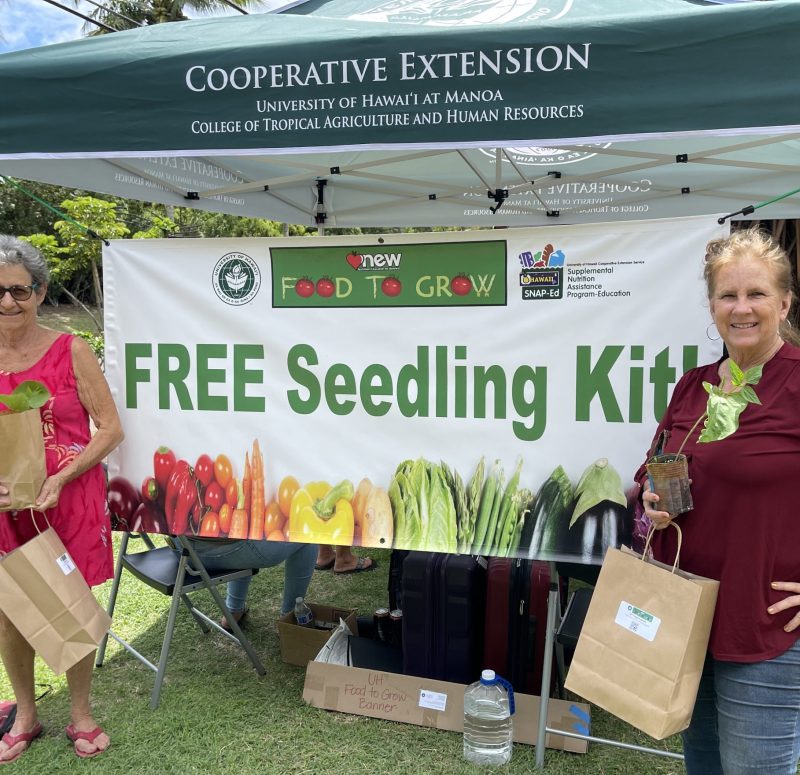 Two people with seedling kits in front of banner